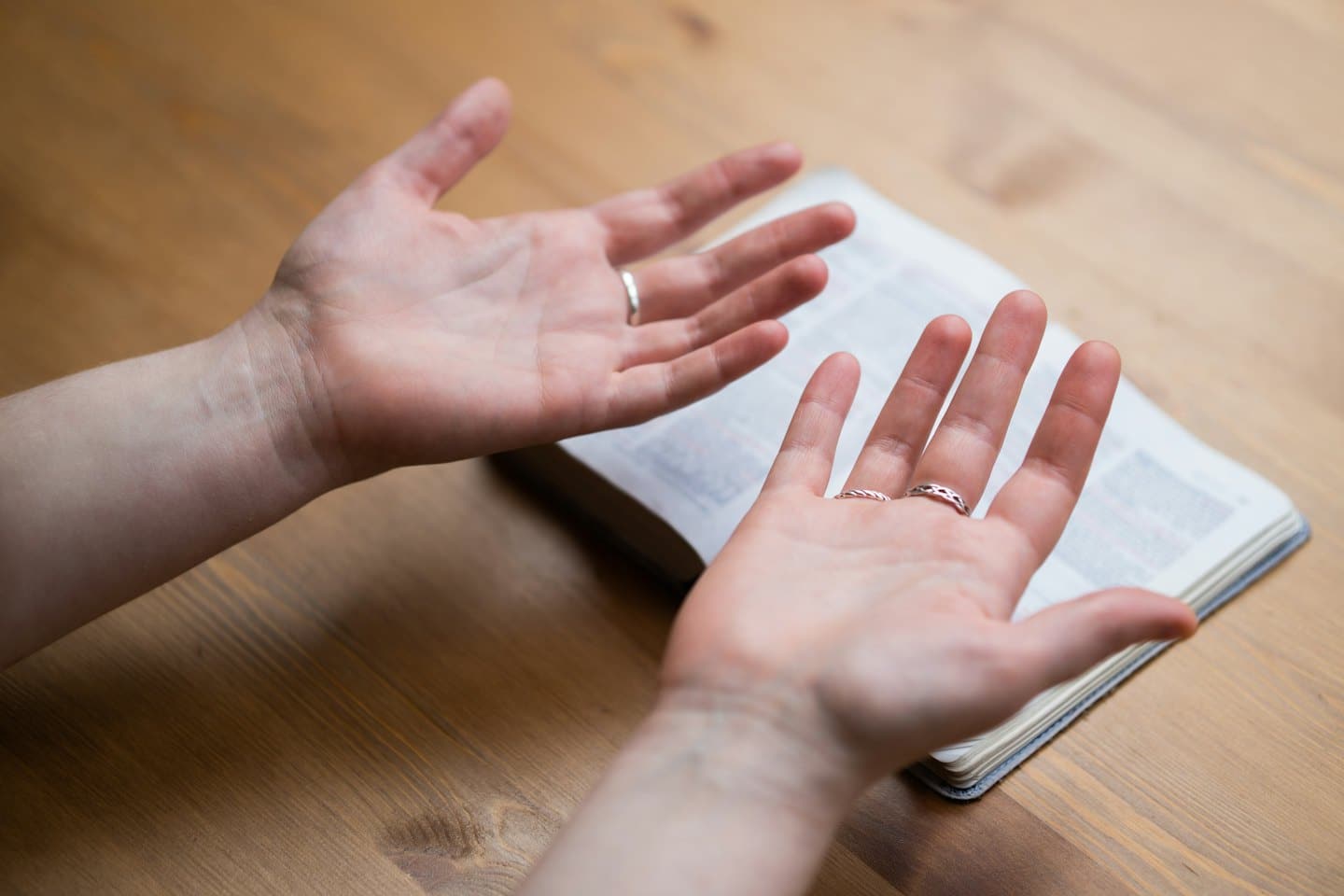 Hands held palms up over an open book on a table.